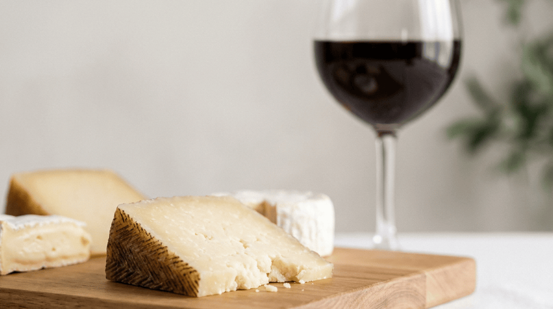 Cheese wedges on a wooden board beside a glass of red wine.