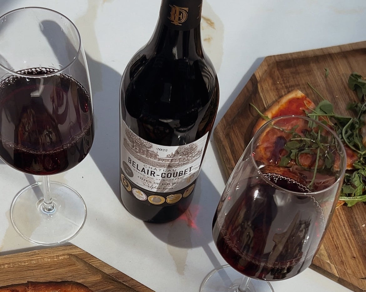 Two glasses of red wine, a bottle of wine, and a small pizza on a white table.